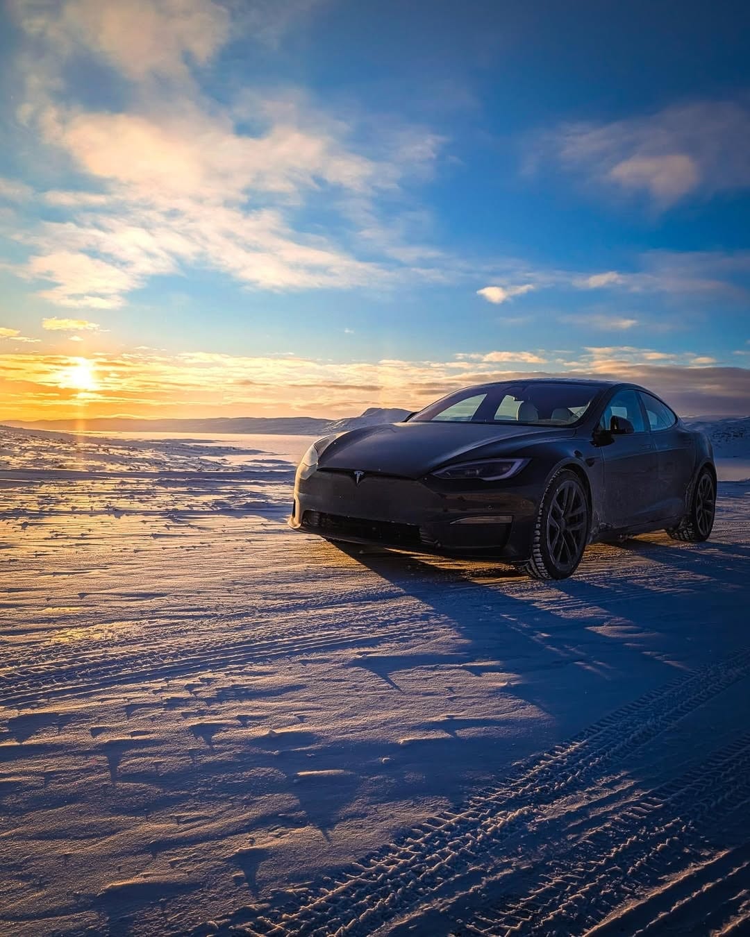 Black Tesla on a snowy Norway road at sunrise, tire tracks in the foreground